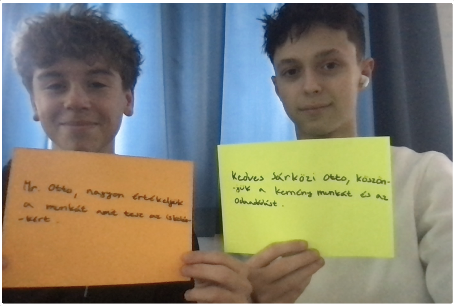 Two AIS Budapest students hold handwritten thank-you letters in Hungarian to a school maintenance worker — part of the gratitude project from the Foundations of Leadership for Impact course.