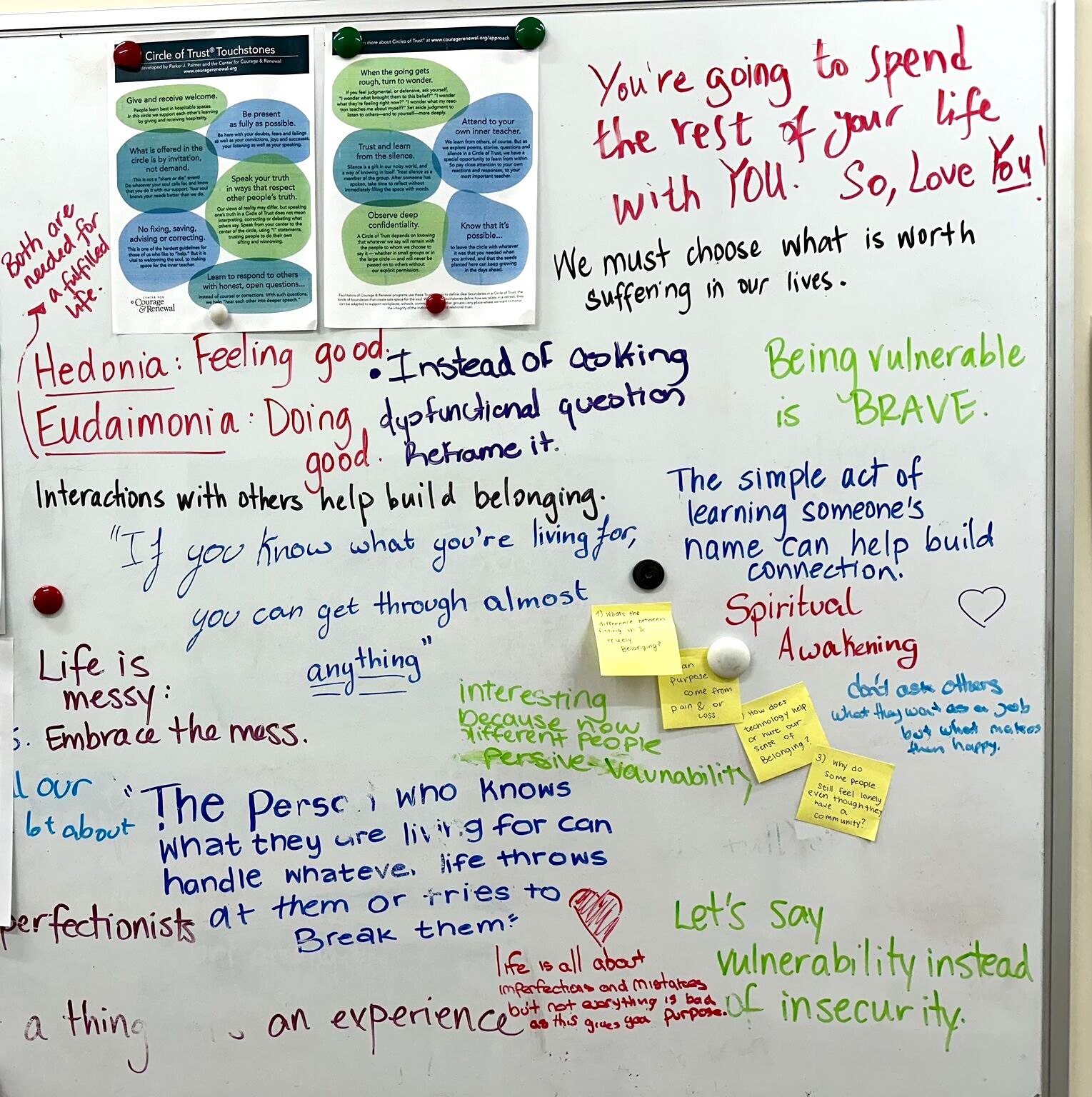 A whiteboard covered in handwritten student reflections and motivational quotes in marker, with pinned posters and sticky notes.